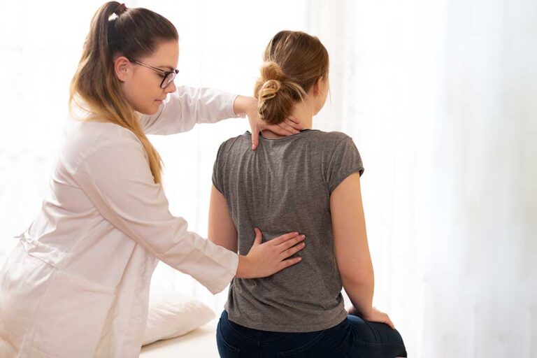 Person resting in a dim room while a clinician assesses neck and shoulder tension.